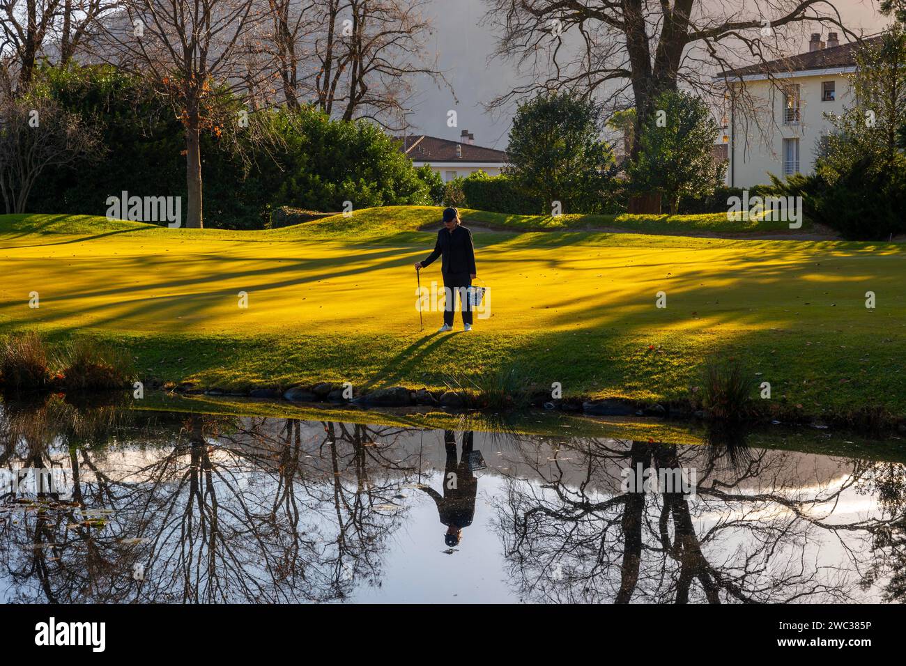 Weibliche Golferin reflektiert und sucht nach Golfbällen im Wasserteich auf dem Golfplatz in der Schweiz Stockfoto