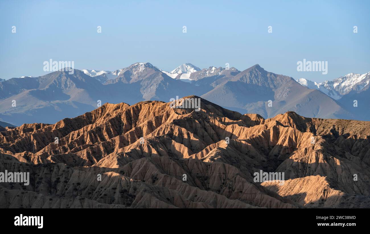 Sonnenaufgang über Canyons, Tian Shan Berge im Hintergrund, erodierte hügelige Landschaft, Badlands, Tal der vergessenen Flüsse, in der Nähe von Bokonbayevo Stockfoto