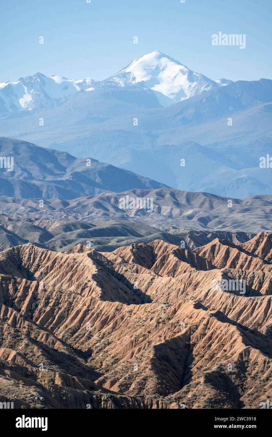 Canyons in Wüstenlandschaft, Berge des Tian Shan im Hintergrund, erodierte hügelige Landschaft, Badlands, Tal der vergessenen Flüsse, in der Nähe Stockfoto