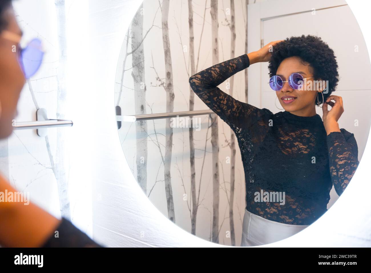 Afrikanische Frau mit Sonnenbrille, die sich vor dem Spiegel auf eine Nachtparty vorbereitet Stockfoto