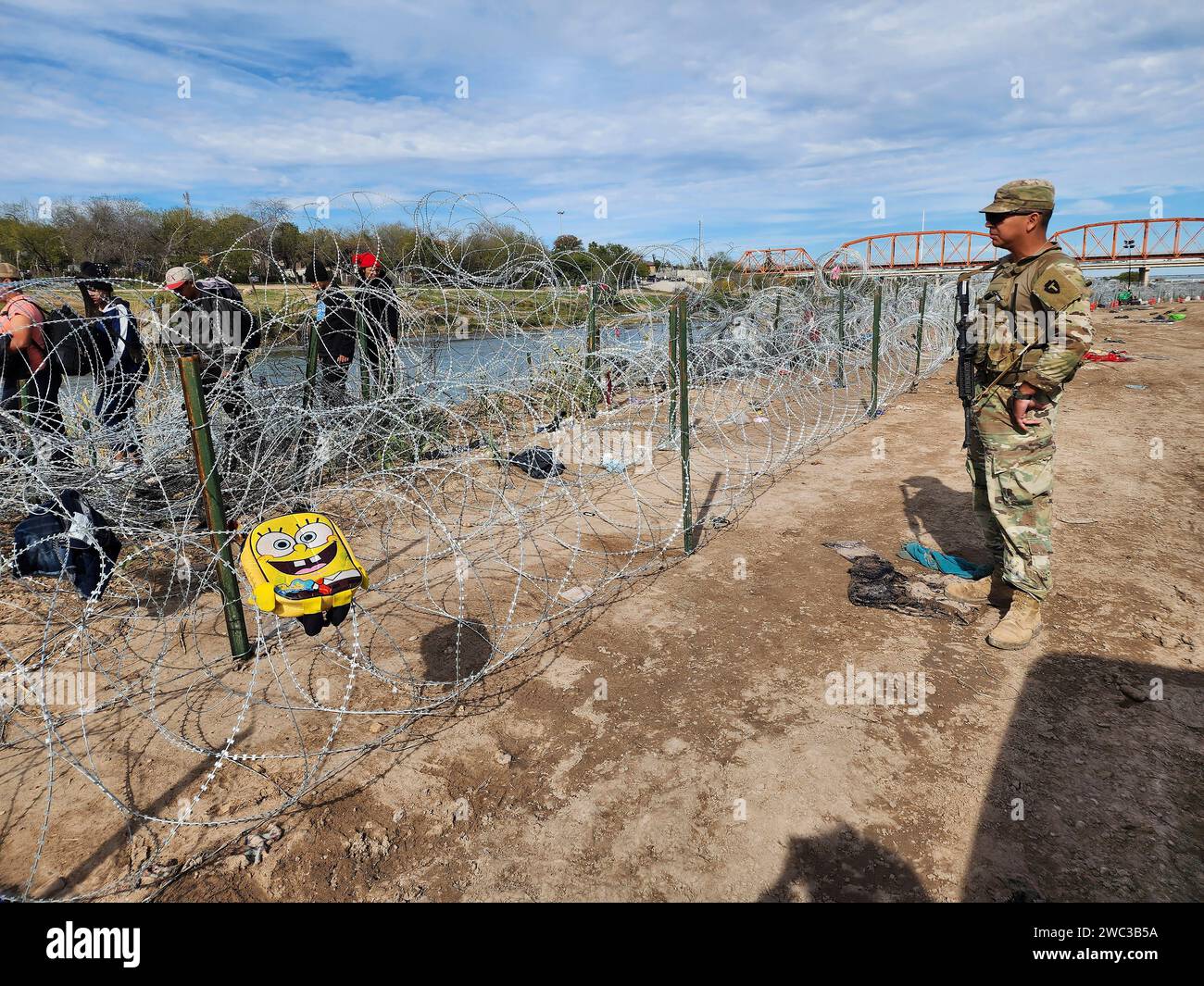 Eagle Pass, Usa. Dezember 2023. Texas Army National Guardsmen beobachten, wie Migranten beim Überqueren des Rio Grande an der texanisch-mexikanischen Grenze am 19. Dezember 2023 im Eagle Pass, Texas, auf Stacheldraht stoßen, der den Zugang blockiert. Die Soldaten handeln auf Befehl des Gouverneurs von Texas im Rahmen der staatlich geförderten Operation Lone Star. Quelle: 1SG Suzanne Ringle/Texas National Guard/Alamy Live News Stockfoto