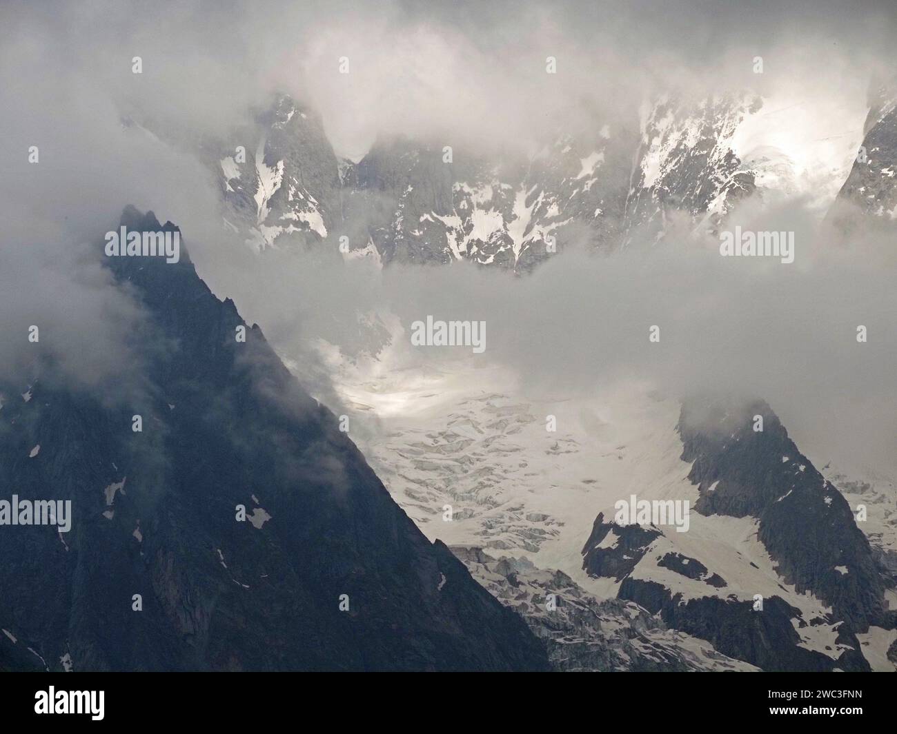 Stimmungsvolle Aussicht auf die italienischen Alpen über Courmayeur mit schwachem Sonnenschein, der die niedrigen Wolken über die schneebedeckten Gipfel und Felsen durchzieht Stockfoto