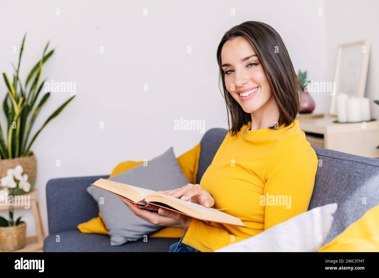 Lächelndes Porträt einer jungen schönen Frau, die ein Buch auf der Couch liest Stockfoto