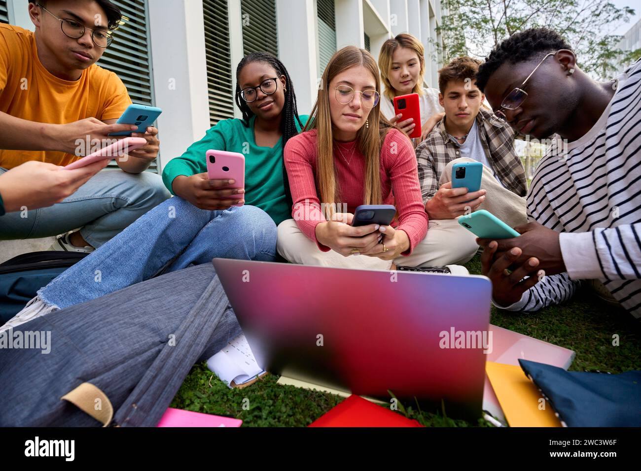 Eine Gruppe junger multirassischer Universitätsstudenten tauchte abhängig von ihrer Mobilzellentechnologie ein Stockfoto
