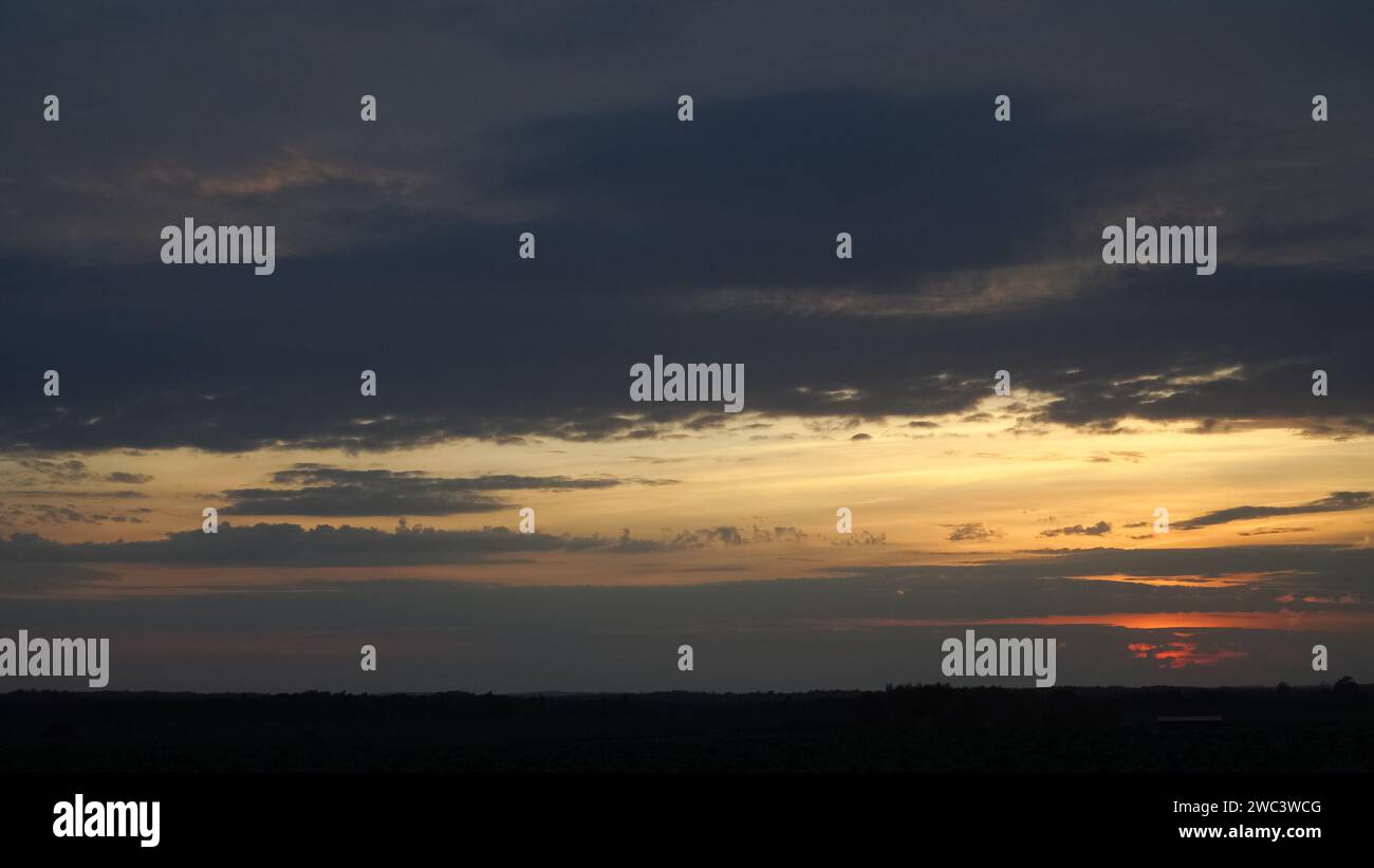 Panoramablick auf den goldenen Sonnenuntergang mit dramatischen, dunkelgrauen Wolken. Die wunderschöne abendliche Landschaft zeigt eine sichtbare Horizontlinie auf einer Ebene bei Stockfoto