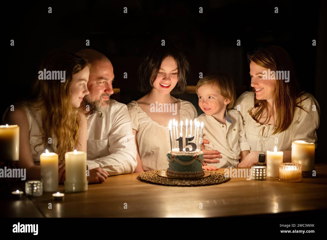 Niedliches 15-jähriges Mädchen, das sich wünscht, bevor es Kerzen auf ihre Geburtstagskuche bläst. Fünfköpfige Familie feiert Kindergeburtstag. Geburtstags-Traditionen Stockfoto