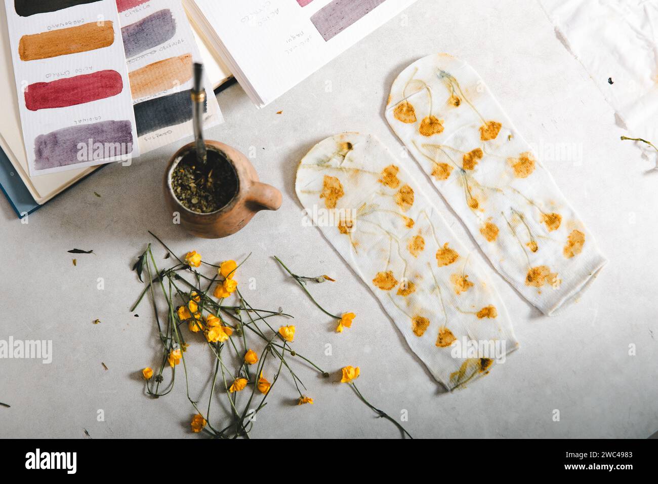 Draufsicht auf einen textilen Künstlertisch mit botanischem Druck auf Naturfaser-Kleidung. Künstlerisch gefärbte Socken. Yerba Mate Stockfoto