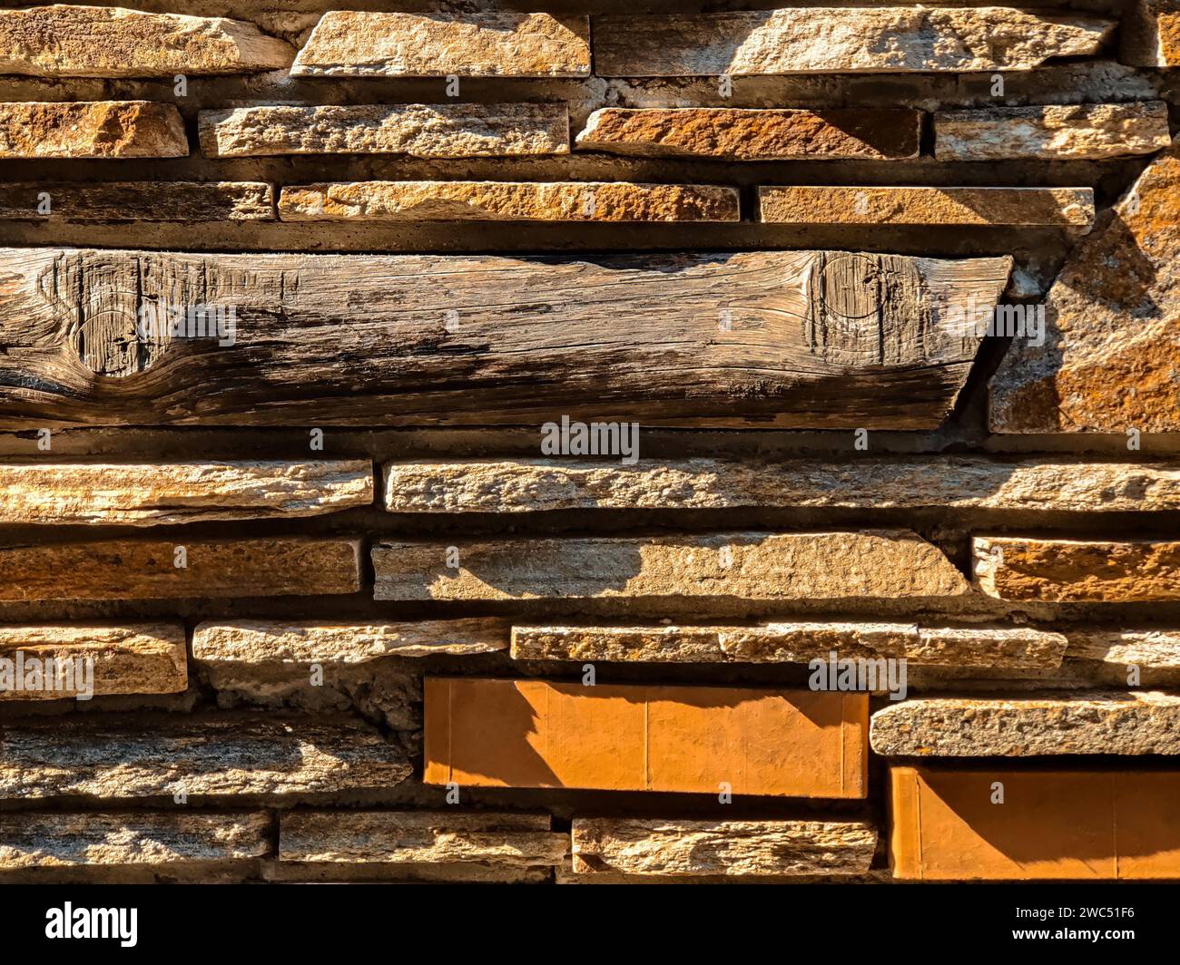 Die Mauerwerk-Wand besteht aus grauem wildem Flachstein, gemischt mit Ziegeln und einer Holzstange. Seitliches natürliches Sonnenlicht. Kopierbereich. Nahaufnahme. Stockfoto