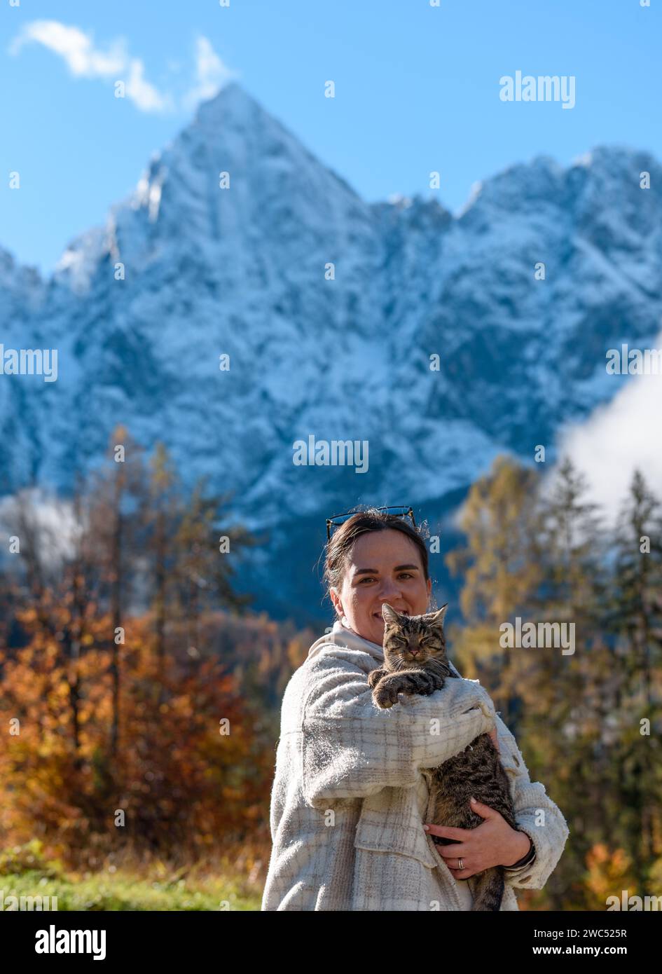 Ein Porträt einer glücklichen Kaukasierin, die eine niedliche Katze mit einem Berggipfel im Hintergrund hält Stockfoto