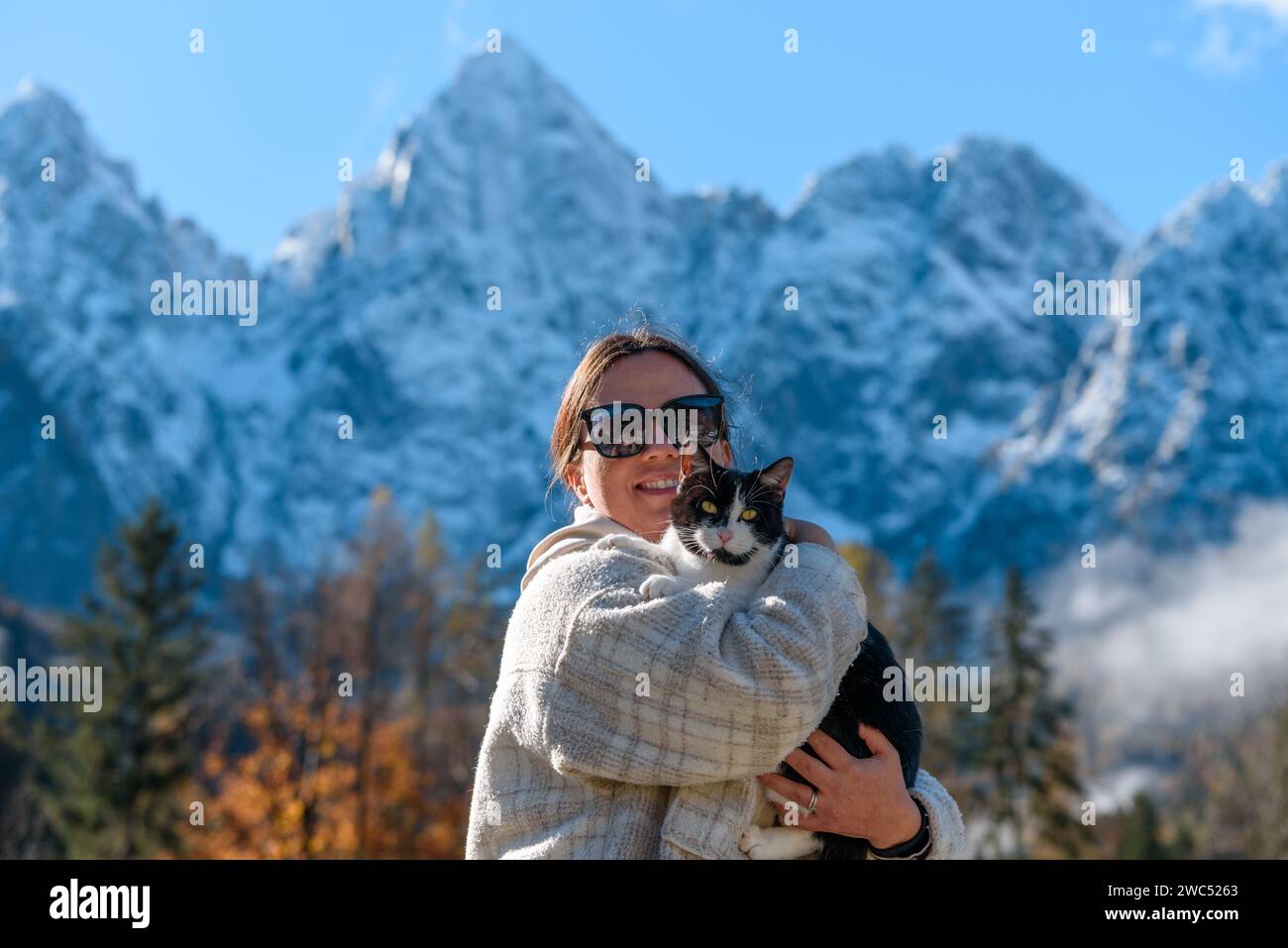 Ein Porträt einer glücklichen Kaukasierin, die eine niedliche Katze mit einem Berggipfel im Hintergrund hält Stockfoto