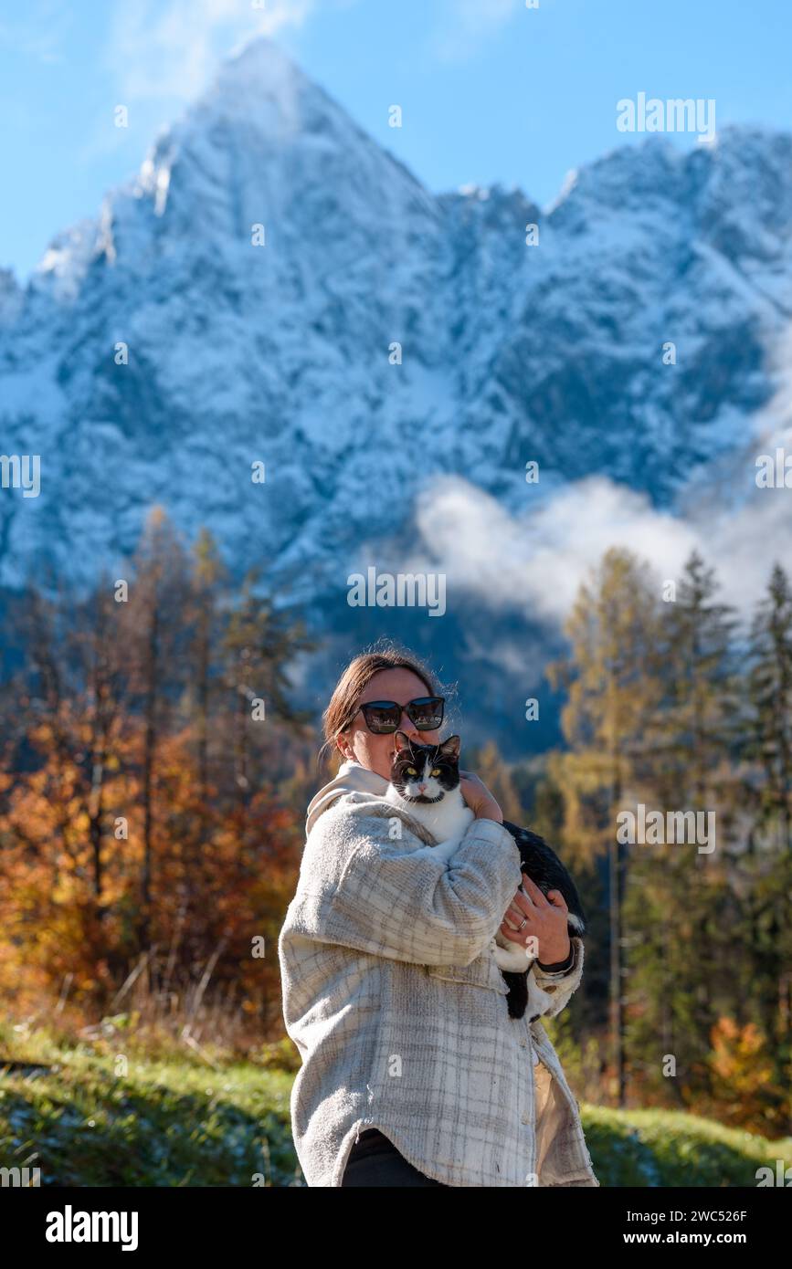 Ein Porträt einer glücklichen Kaukasierin, die eine niedliche Katze mit einem Berggipfel im Hintergrund hält Stockfoto