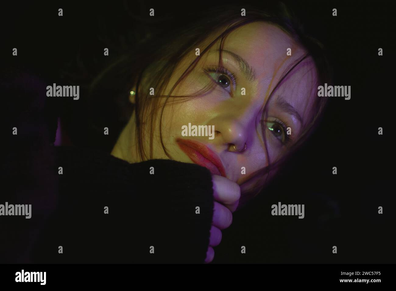 Eine atemberaubende Frau mit leuchtendem rotem Lippenstift und einer eleganten schwarzen Jacke ist in einem schwach beleuchteten Raum zu sehen Stockfoto