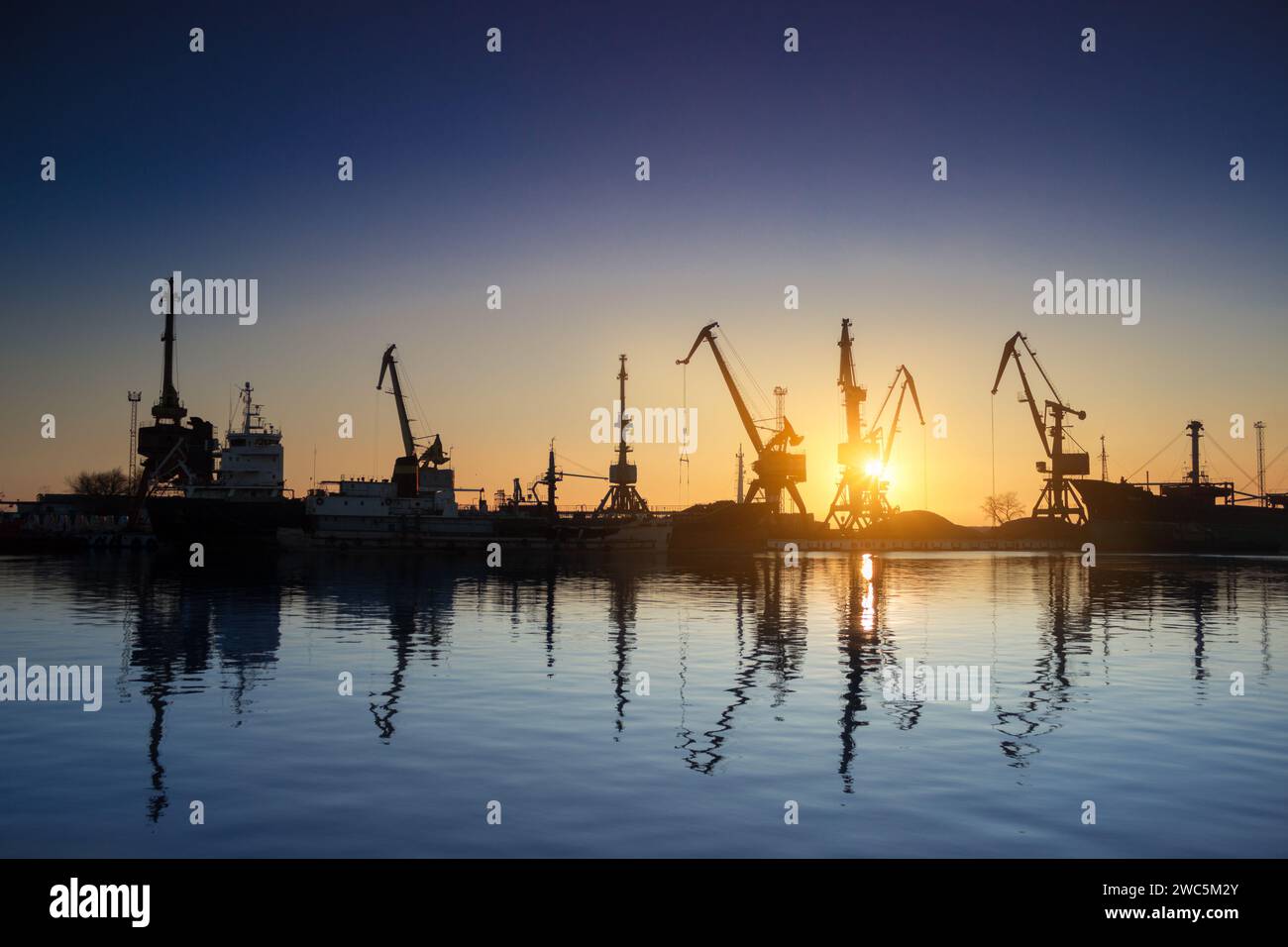Sonnenuntergang Silhouetten Frachtschiffe, Kräne am Seehafen. Industrie lädt Fracht am Dock. Handel, Verkehrsinfrastruktur. Maritime Logistik, global Stockfoto