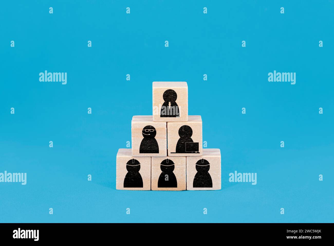 In Pyramidenform gestapelte Holzblöcke mit jeweils einem Symbol, das verschiedene Rollen in einer Unternehmenshierarchie darstellt, vor blauem Hintergrund Stockfoto
