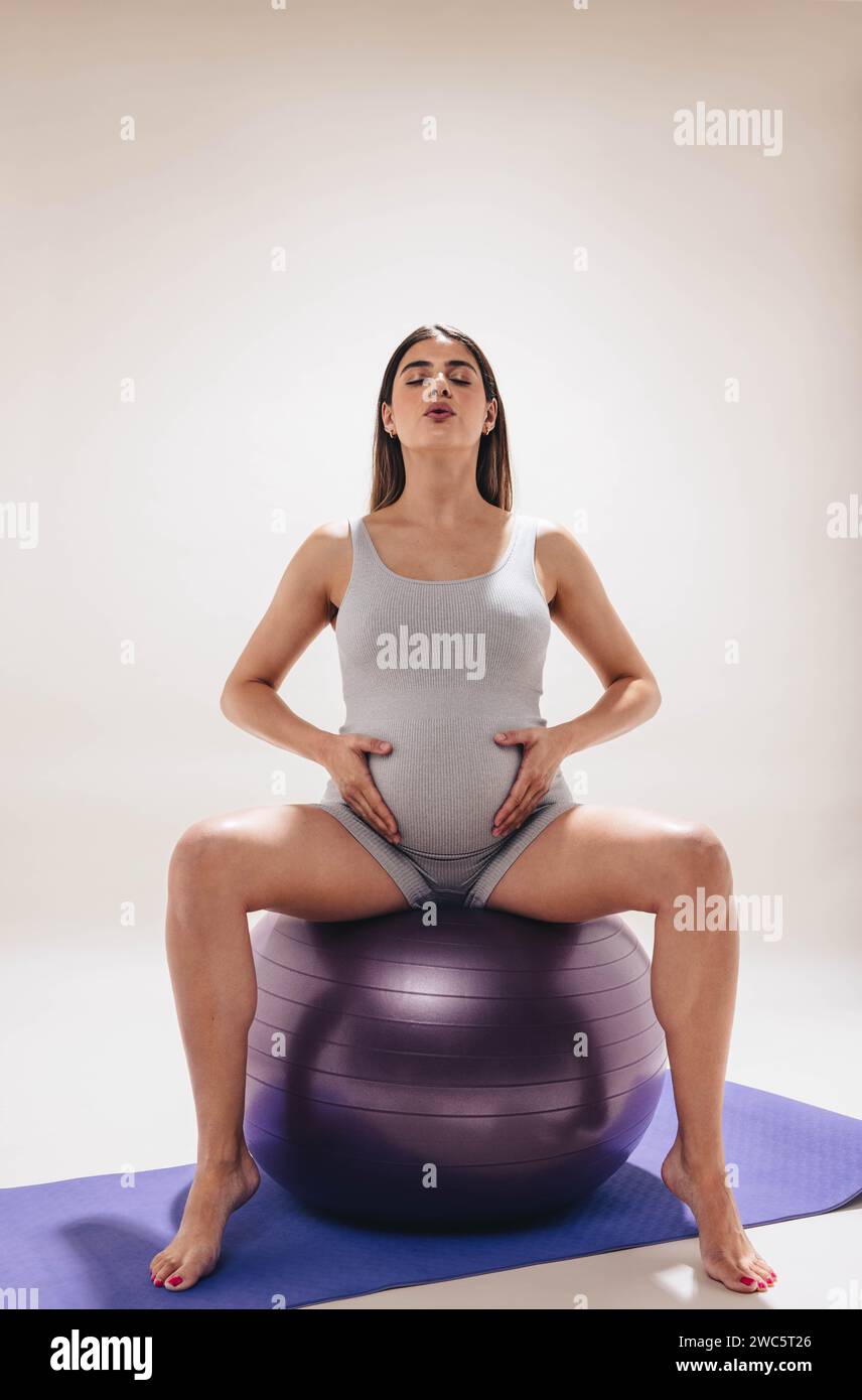 Schwangere Frau übt pränatalen Yoga, sitzt auf einem Trainingsball in einem Studio. Sie konzentriert sich auf ihr Wohlbefinden und behält Kraft und Stabilität. Th Stockfoto