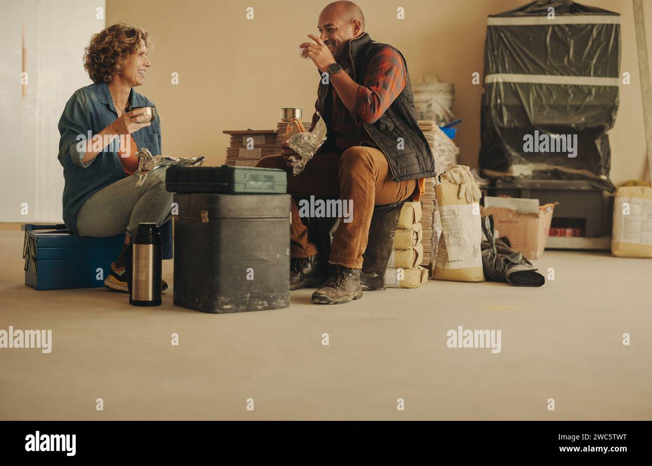 Ein verheiratetes Paar, das an einem Renovierungsprojekt mitarbeitet. Sie halten inne, um sich zu unterhalten, und genießen Kaffee. Der reife Ehemann und die Frau diskutieren in Teamarbeit Stockfoto