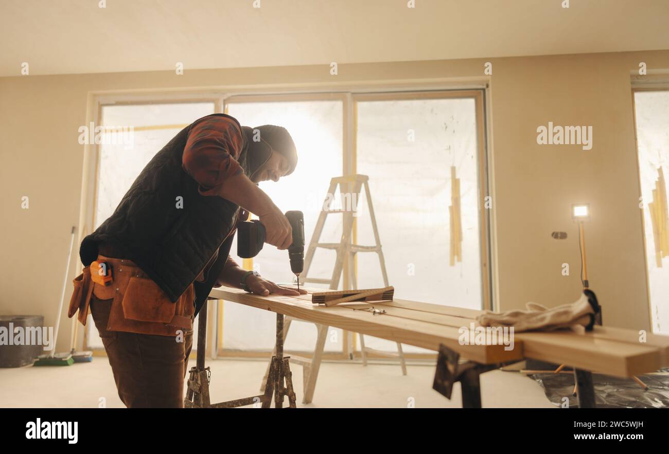 Generalunternehmer, der eine Küche in einem Haus renoviert. Bauarbeiter, der einen Bohrer auf Holzdielen für die Montage von Sockelleisten verwendet. Eine qualifizierte Arbeit Stockfoto