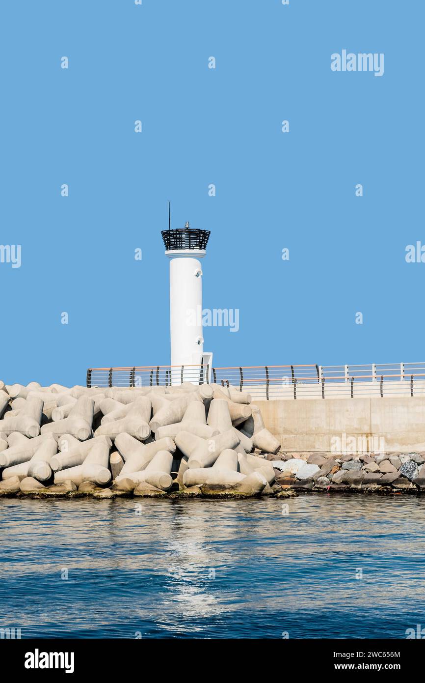 Weißer Leuchtturm auf Betonpier vor klarem blauem Himmel Stockfoto