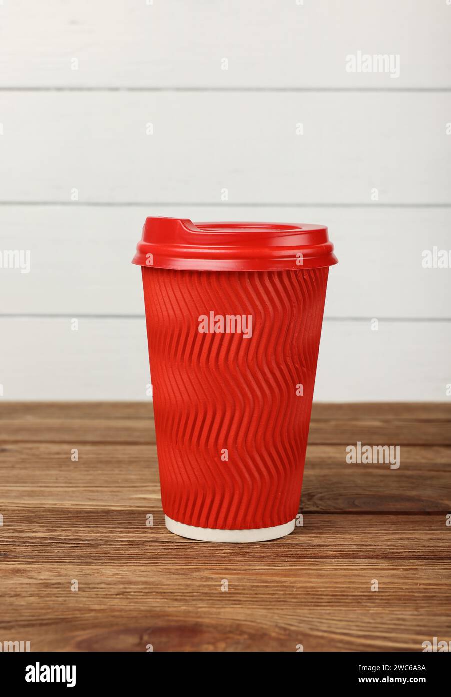 Schließen Sie die große rote Papierkaffee- oder Teetasse auf braunem Holztisch über weiß gestrichener Wand im Coffee-Shop-Einzelhandel Stockfoto