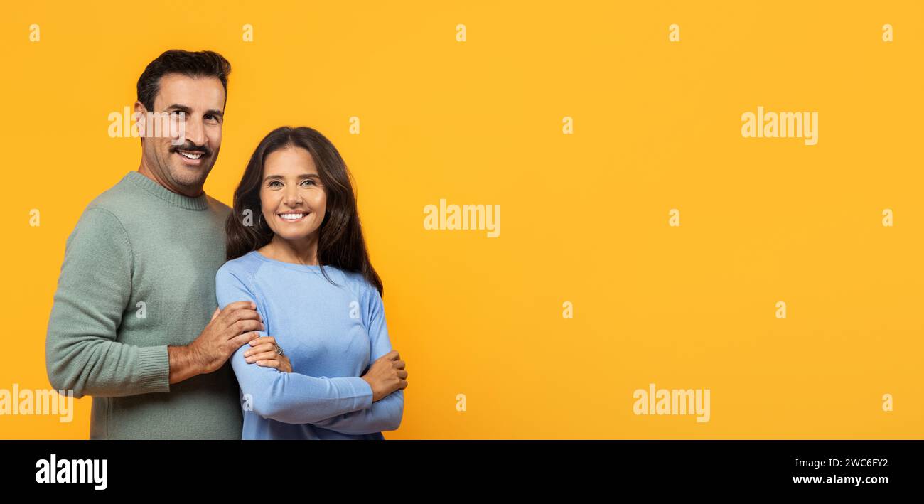 Ein lächelnder Mann und eine Frau in koordinierten Outfits umarmen sich herzlich und schauen zur Seite Stockfoto