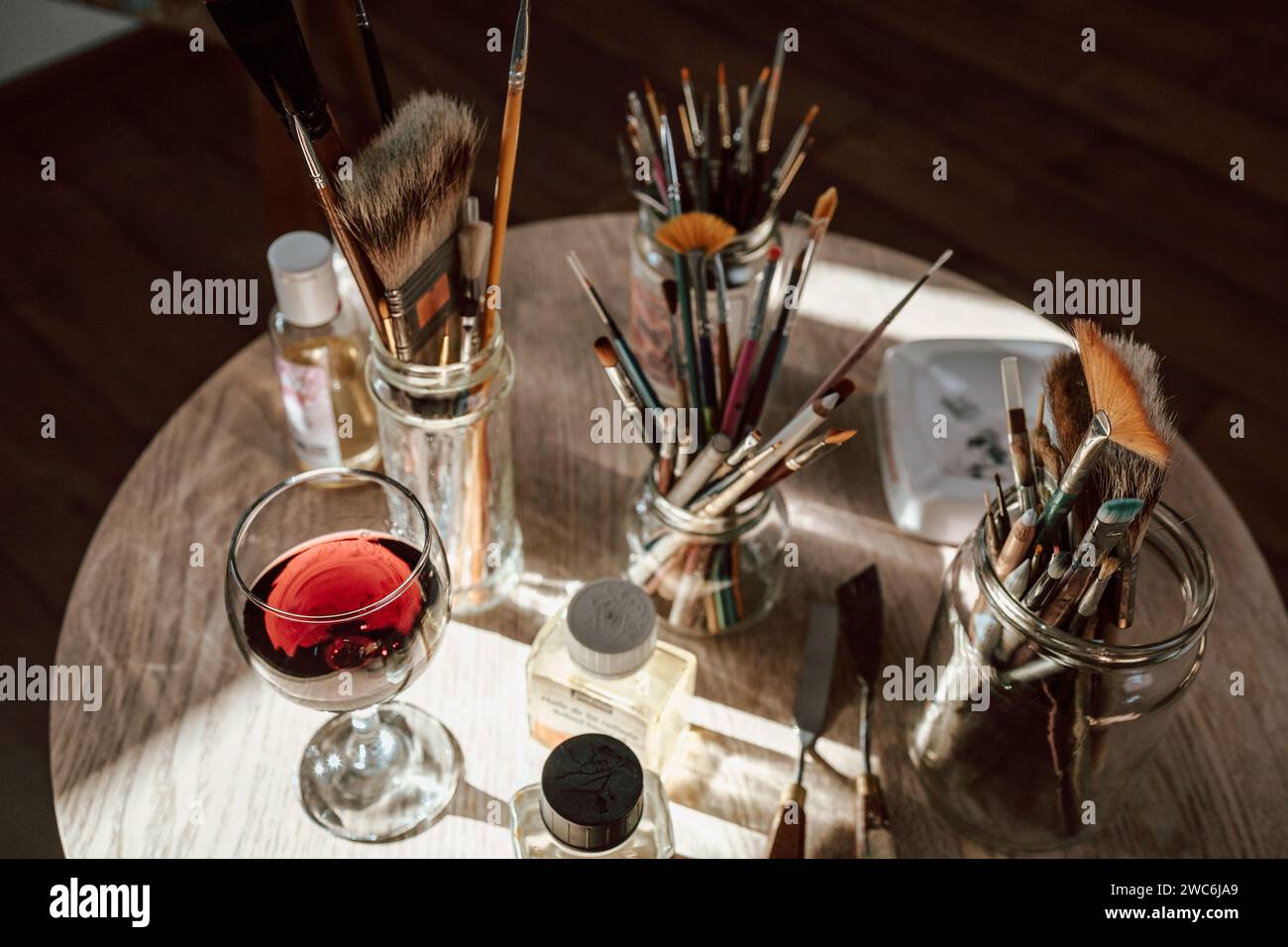 Draufsicht auf einen Tisch mit Malwerkzeugen, Pinseln, Öl, Farben und Rotweinglas Stockfoto