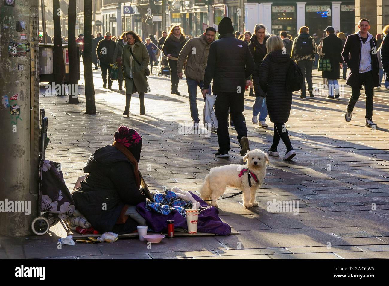 Anonyme Straßenbettlerin mit ihrem Hund, sitzt in der Buchanan Street, Glasgow, Schottland, während Fußgänger vorbeilaufen. Stockfoto