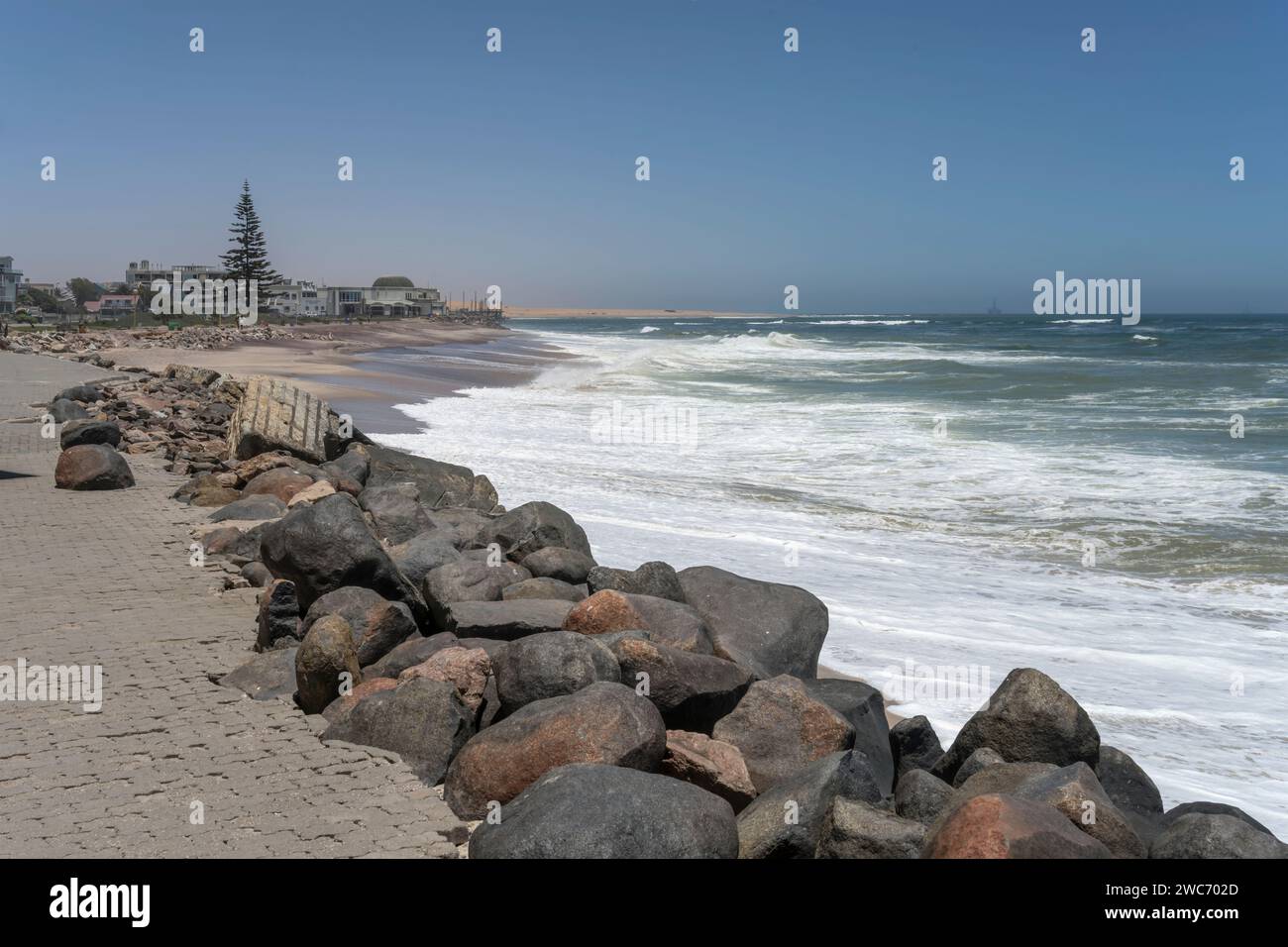 Stadtansicht mit Wellen des Atlantiks am Sandstrand der historischen Stadt, im Hintergrund gelbe Dünen, aufgenommen im hellen Licht des späten Frühlings bei Swakopomund, äh Stockfoto