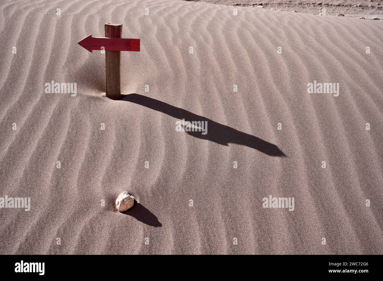 Holzpfeilkreuz mit Schatten und einem isolierten Felsen auf einer Sanddüne. San Pedro de Atacama, Chile. Stockfoto