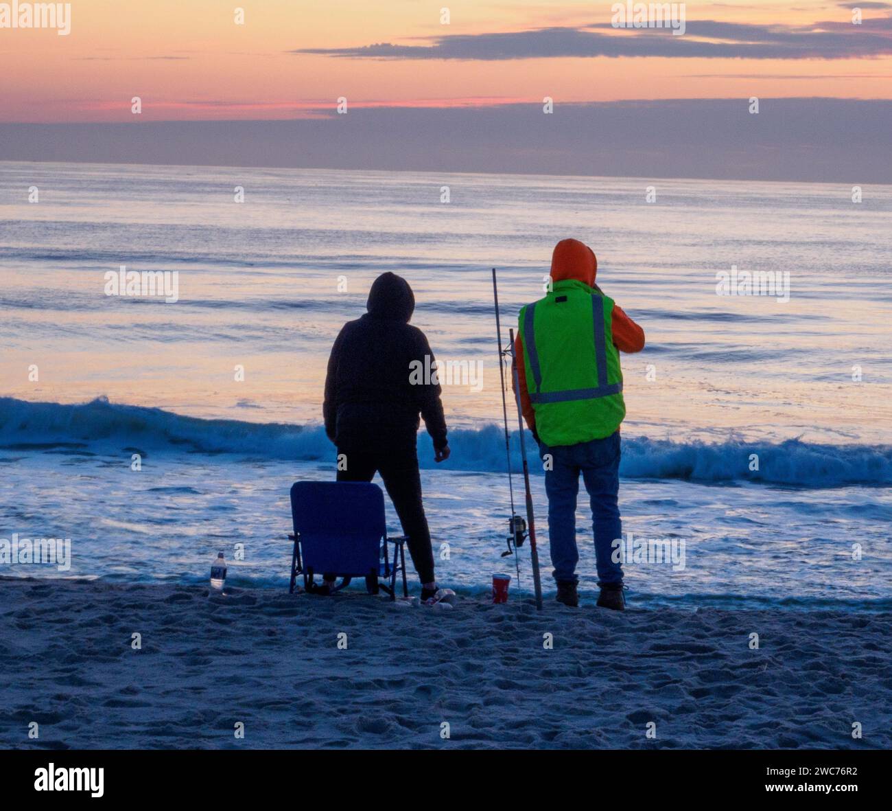 Zwei Individuen stehen am Rande eines Sandstrandes, ihre Blicke auf die riesige Weite des glitzernden blauen Ozeans vor ihnen gerichtet Stockfoto