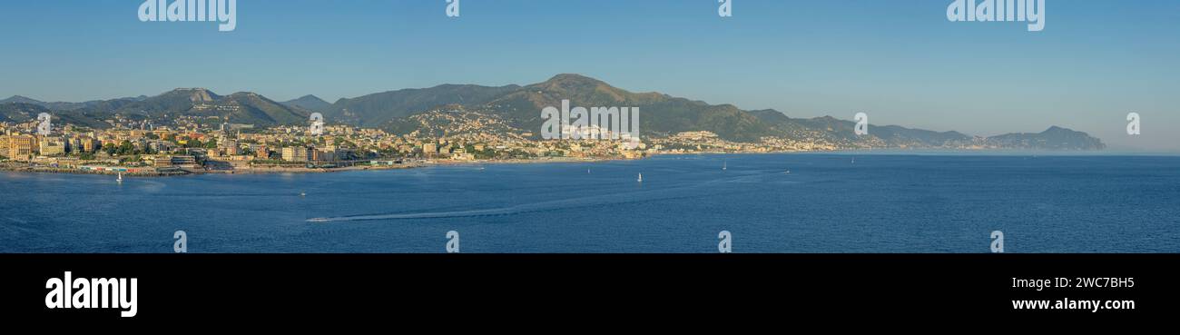 Das verblassende Licht der Dämmerung zieht sich über Genuas weitläufige Küste, wo das Meer auf ein Stadtbild trifft, eingebettet in sanfte Hügel. Die sanfte Kurve von Stockfoto