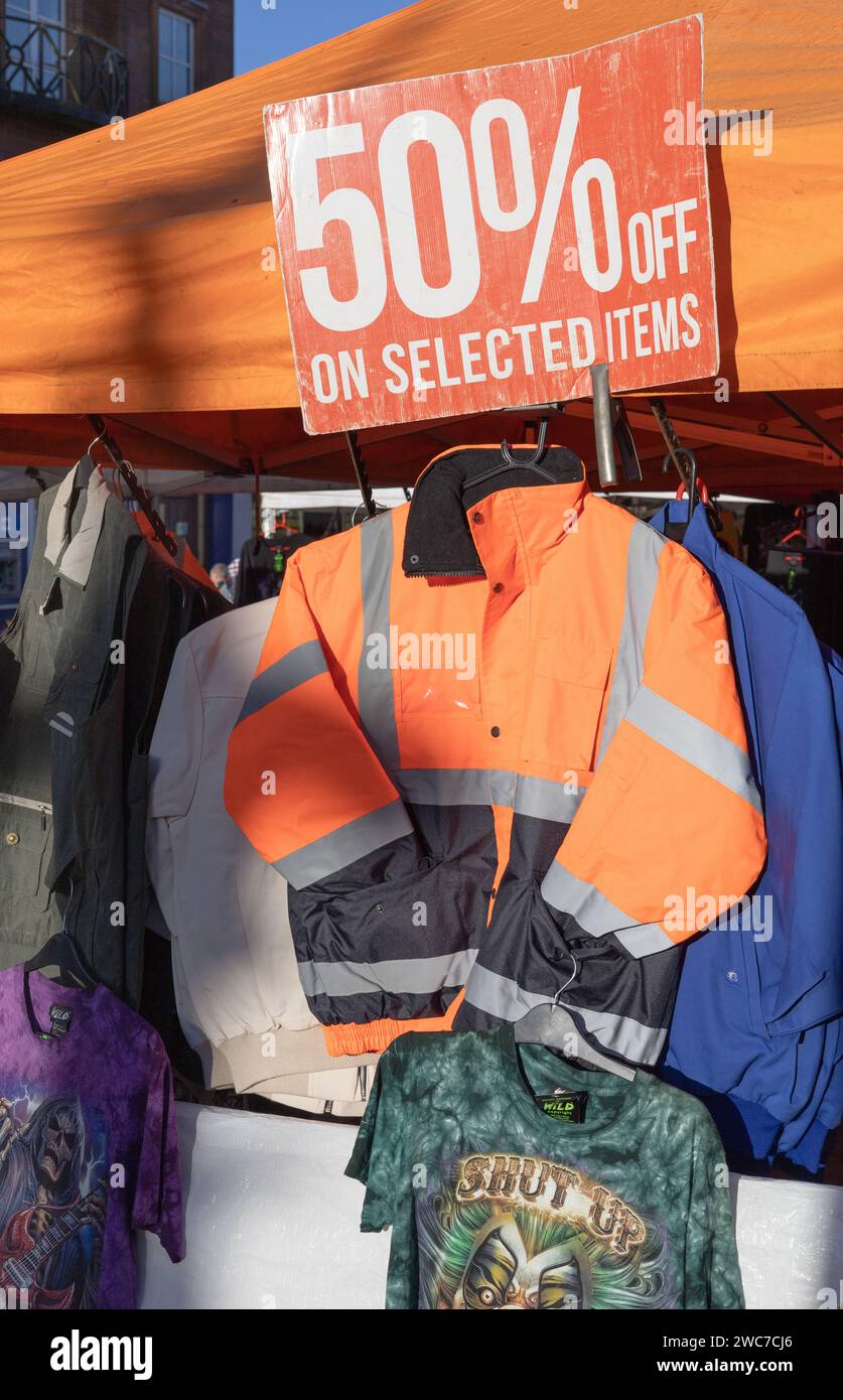 Jacken und T-Shirts zum Verkauf auf einem Open-Air-Markt in Dumfries, Schottland, mit einem Poster, das 50 % Rabatt auf ausgewählte Artikel anzeigt. Stockfoto