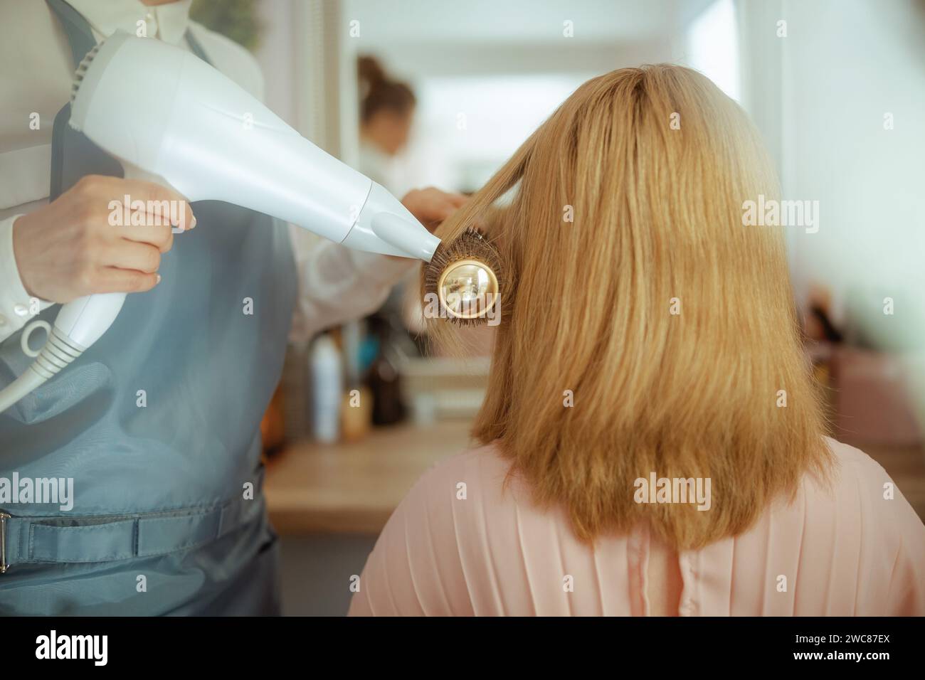 Nahaufnahme einer 40-jährigen Friseurin in einem modernen Schönheitssalon mit Haarbürste und Haarfön für Kunden. Stockfoto
