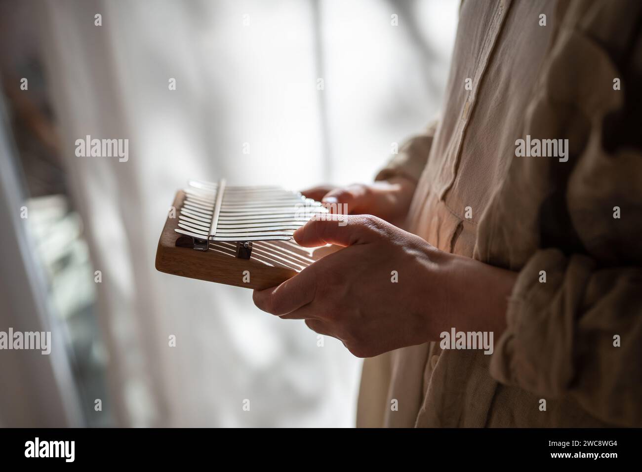 Frauenhände lernen, um Musik auf hölzernem Kalimba zu spielen, die zu Hause in der Nähe des Fensters stehen. Stockfoto