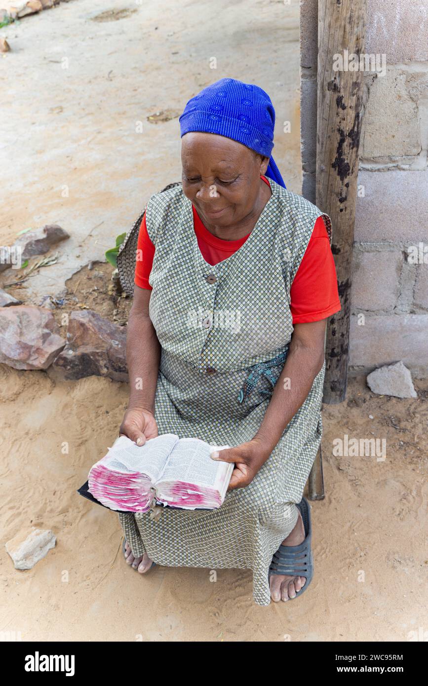 Alte afrikanerin liest die Bibel im Hof, Dorf in Botswana Stockfoto