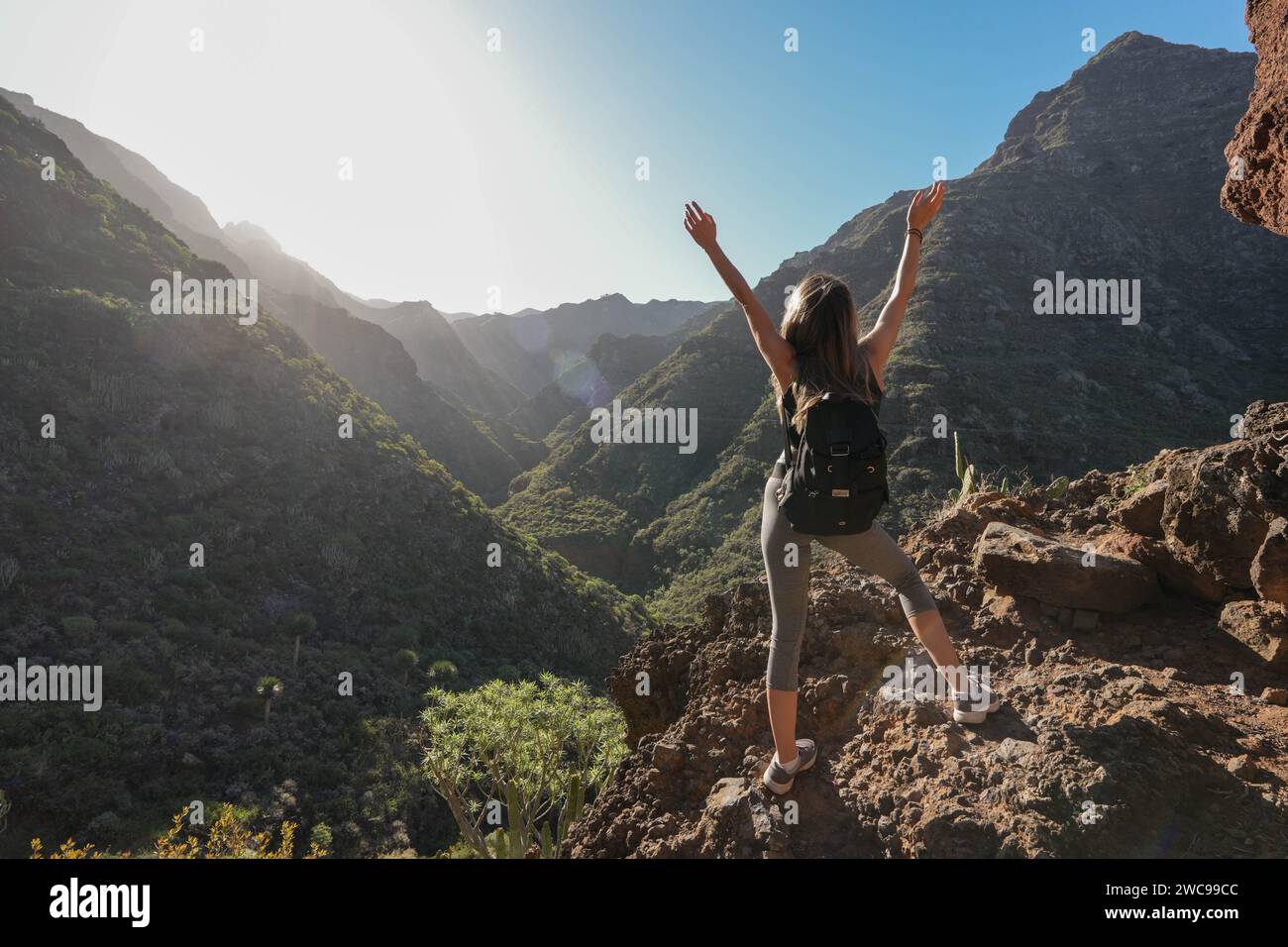 Junger Wanderer, von hinten gesehen, triumphierend mit erhobenen Armen auf dem zerklüfteten Gelände des Anaga-Nationalparks auf Teneriffa. Der Wanderer, angezogen Stockfoto