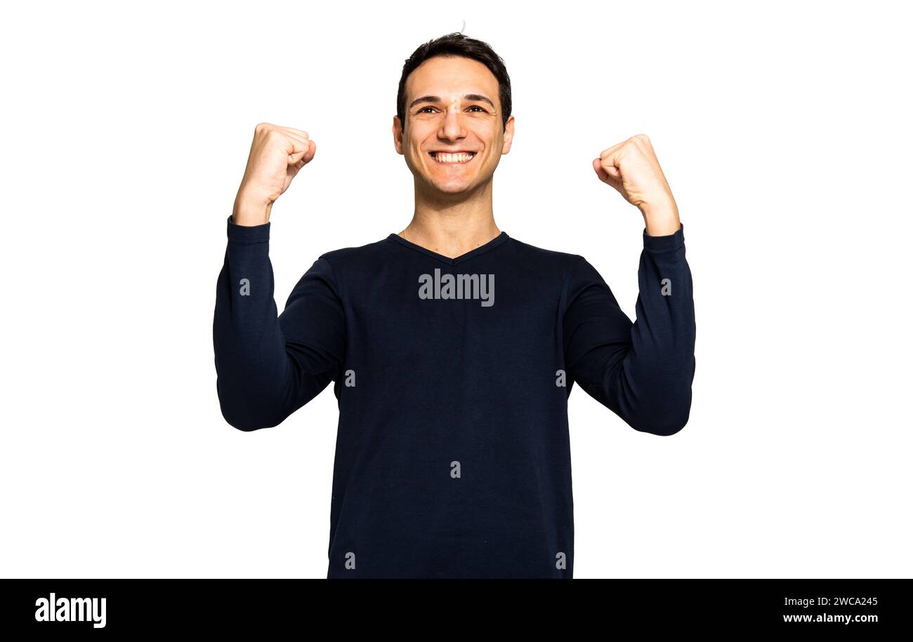 Ein lächelnder junger Mann in einem lässigen Hemd zeigt Kraft und Freude mit erhobenen Fäusten. Stockfoto