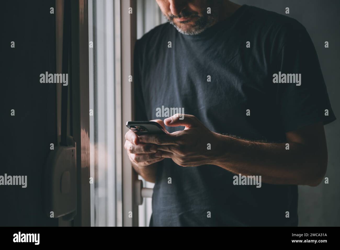 Mann, der Textnachrichten auf dem Handy am Fenster eingibt, niedrige Taste mit selektivem Fokus Stockfoto
