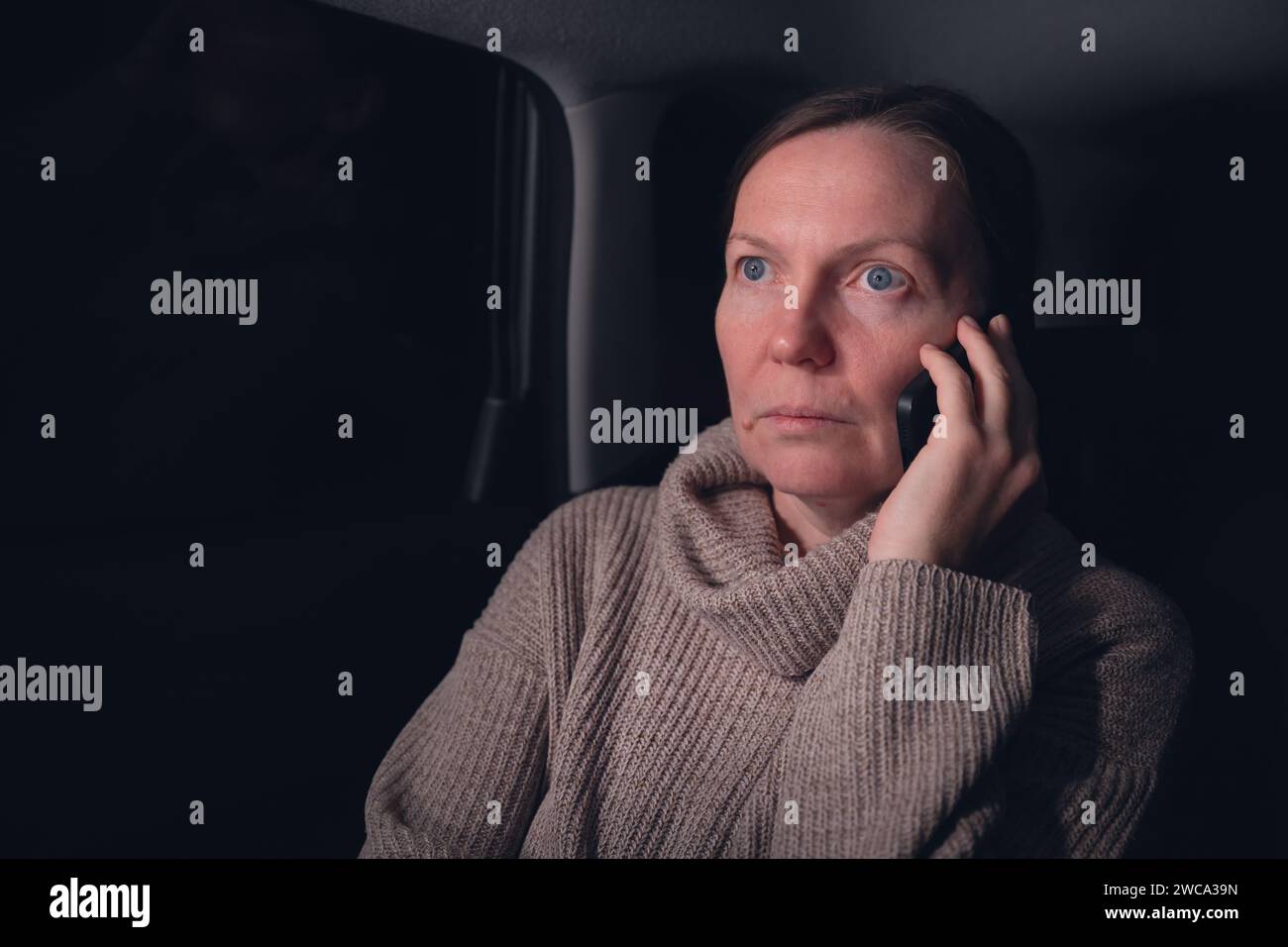 Frau, die auf dem Handy von der Rückbank des Autos auf einem Roadtrip in der Nacht spricht, selektiver Fokus Stockfoto