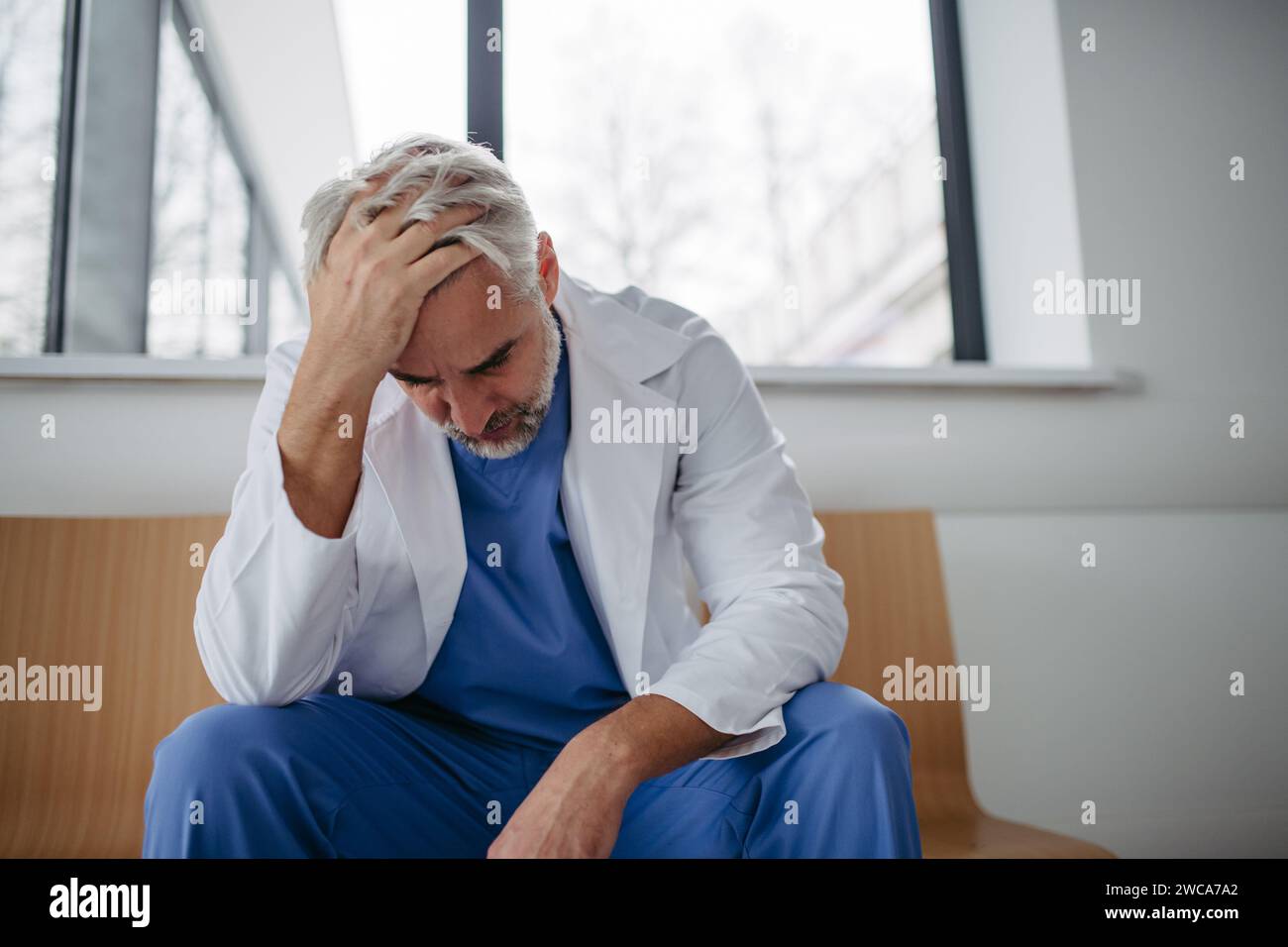 Niedrigwinkelaufnahme eines frustrierten, erschöpften Arztes, der im Krankenhauskorridor sitzt. Das Konzept des Burnout-Syndroms bei Ärzten. Stockfoto