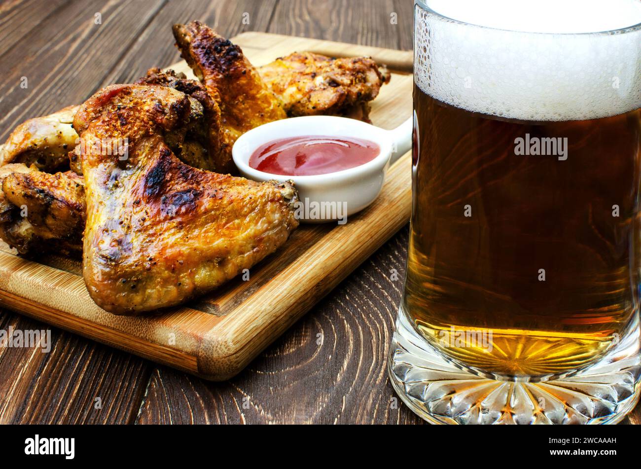 Nahaufnahme einer Mahlzeit bestehend aus gegrillten Hähnchenflügeln, einem Teller Ketchup und einem Glas schaumigem Bier. Hühnerflügel sind goldbraun und lügen Stockfoto
