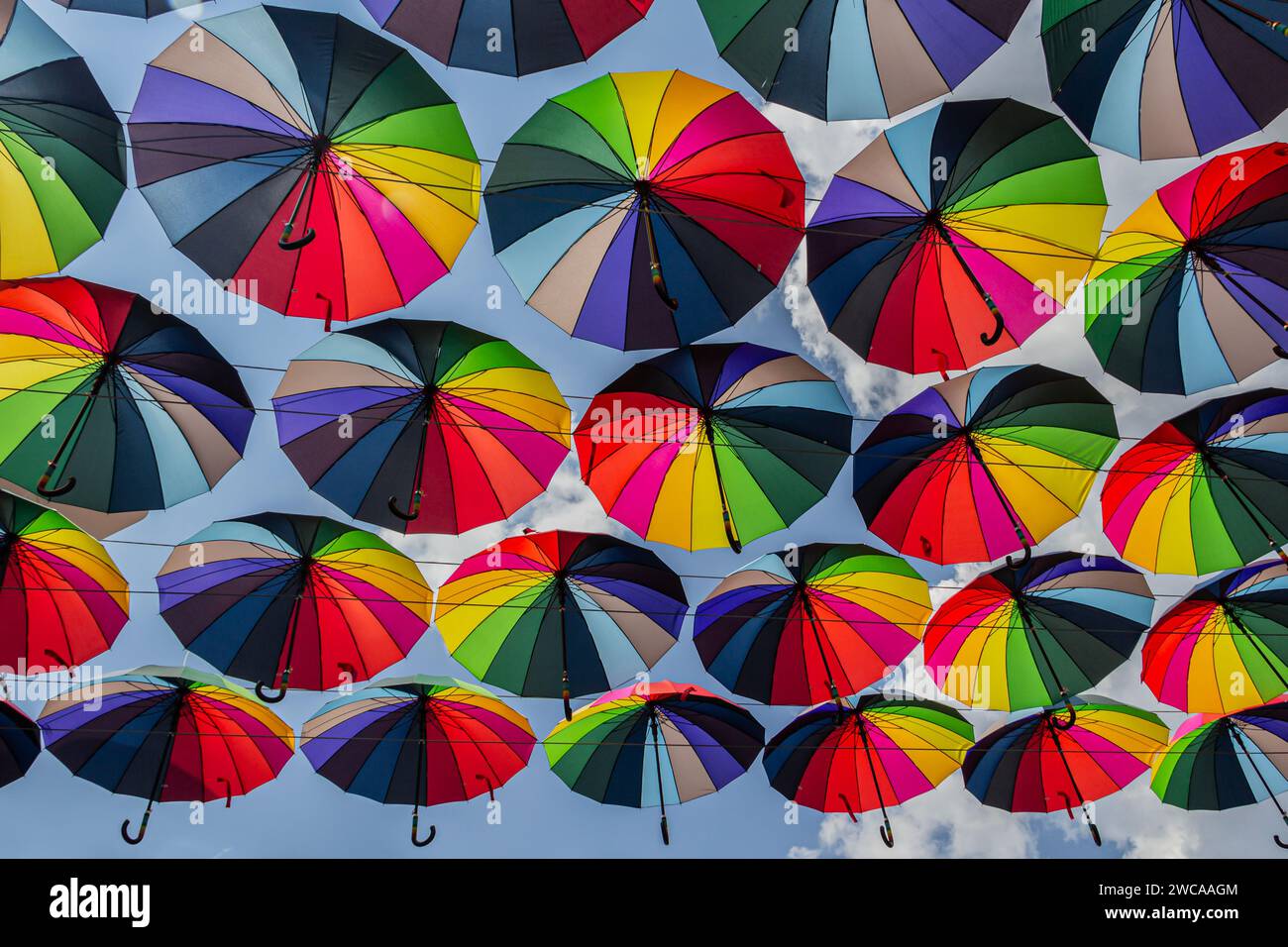 Das Bild fängt den Anblick zahlreicher farbenfroher Regenschirme ein, die in der Luft hängen. Die Regenschirme sind mehrfarbig, jeder mit einer einzigartigen Kombination von en Stockfoto