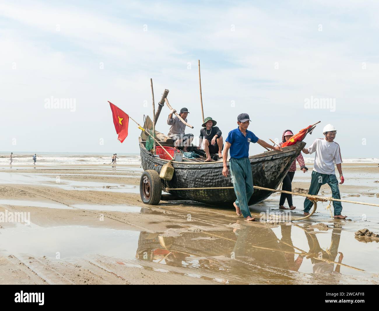 Fischer in Sam Son Beach, Thanh Hoa, Vietnam ziehen am Ende des Arbeitstages ihr Boot an den Strand. Das Boot ist aus Holz gebaut, aber bedeckt Stockfoto
