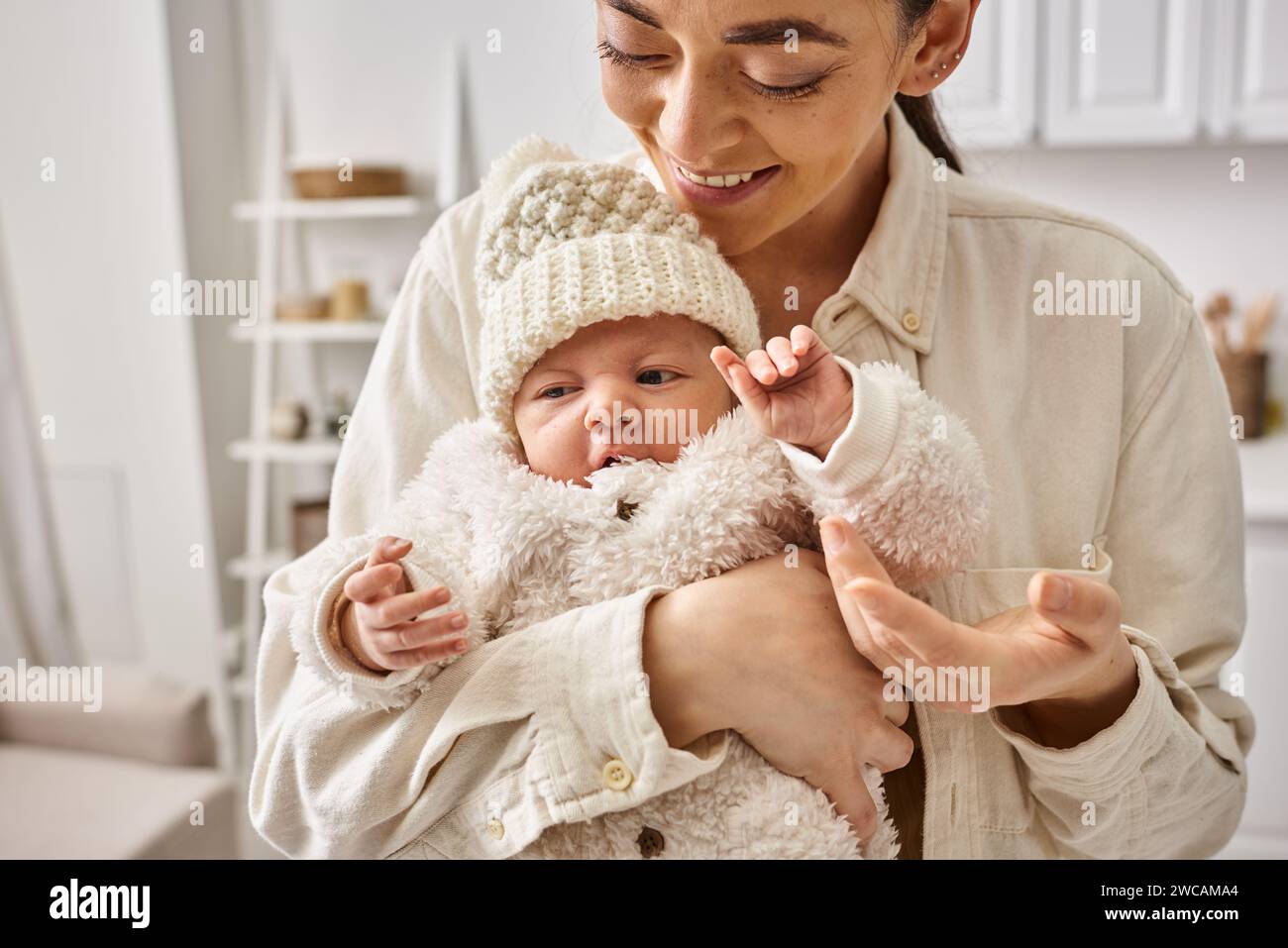 Attraktive, liebevolle Mutter in bequemen Haushaltswaren, die ihren kleinen Jungen warm hält, moderne Erziehung Stockfoto