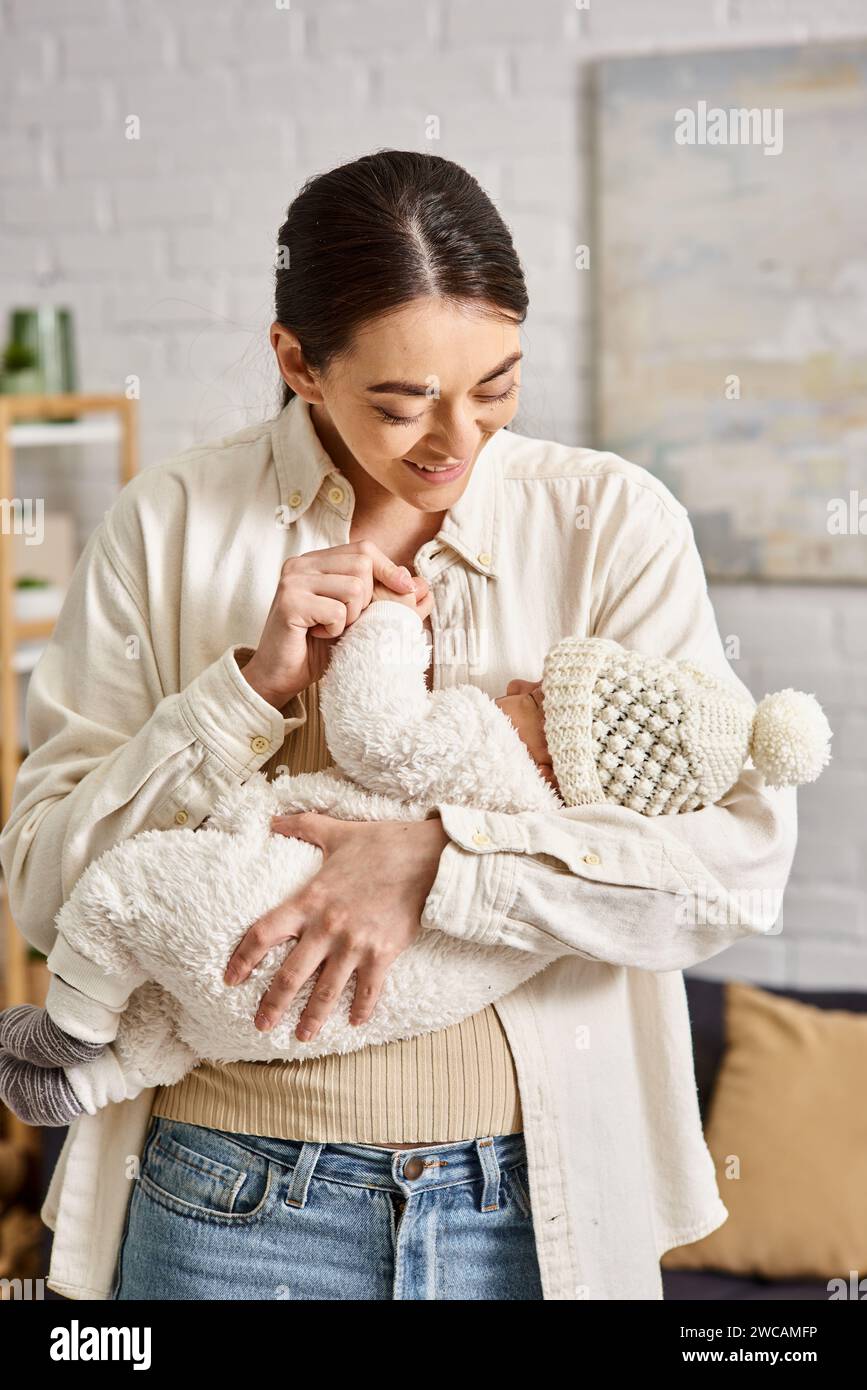 Attraktive, fröhliche Mutter in Hauswäsche, die liebevoll ihren neugeborenen Jungen hält, moderne Erziehung Stockfoto