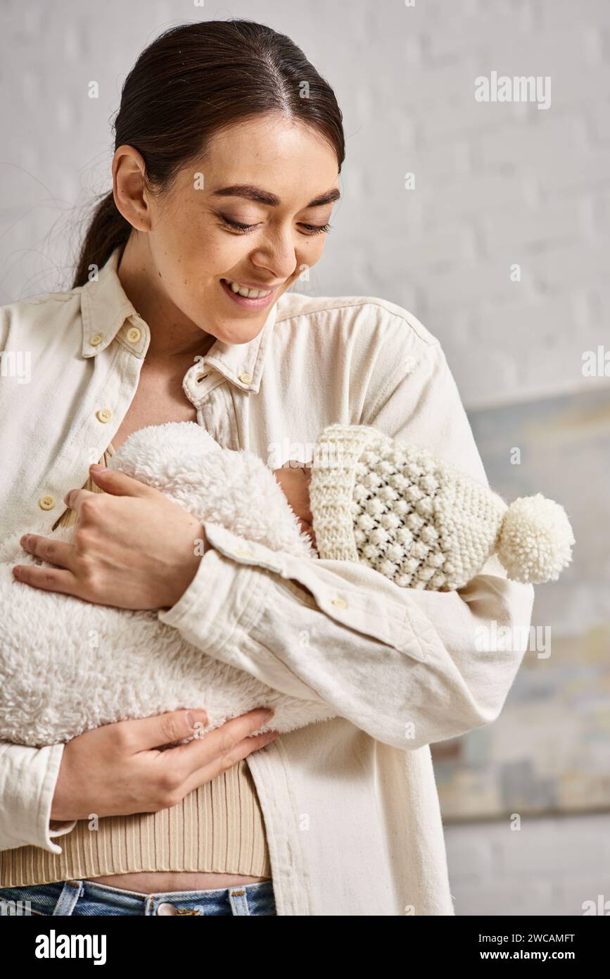 Schöne, fröhliche Mutter in Hauswäsche, die liebevoll ihren neugeborenen Jungen hält, moderne Erziehung Stockfoto