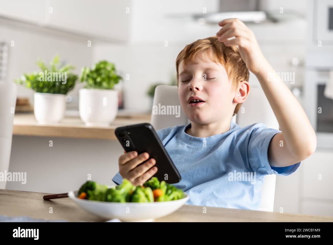 Ein Blick auf einen intelligenten, süßen Jungen, der statt zu Mittag zu essen, Spiele auf seinem Smartphone spielt. Stockfoto