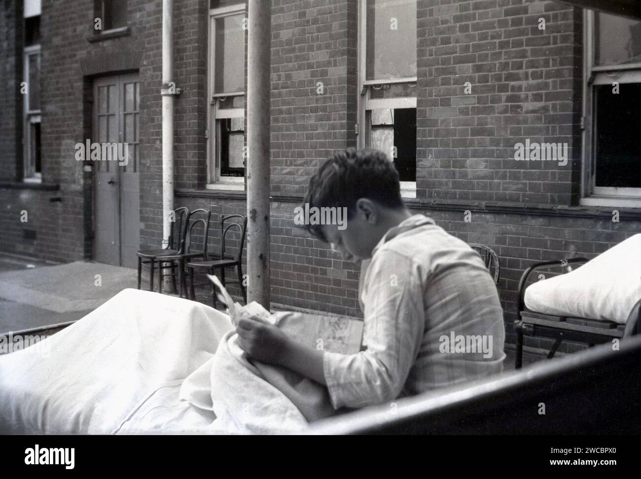 1942, Geschichte, Kriegszeit und ein kleiner Junge in seinem Schlafanzug, der in einem Metallbett sitzt und eine Zeitschrift liest, draußen im Hof des Queen Mary's Hospital, einem Kinderkrankenhaus in Carshalton, Surrey, England, Großbritannien, Stockfoto