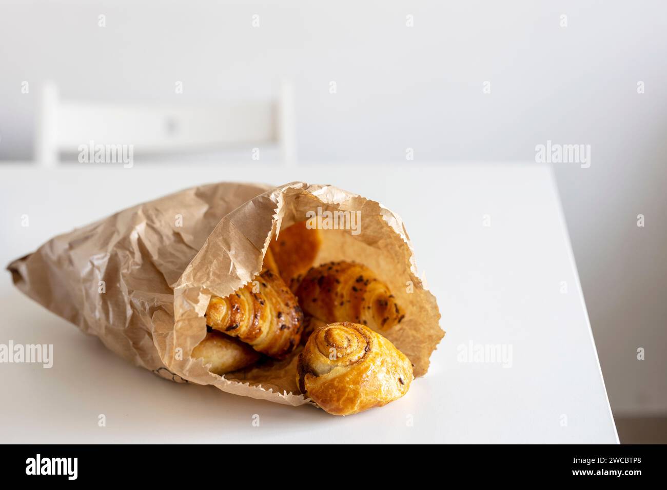 Frisches Gebäck – Croissants mit Schokoladenstückchen, Mohnbrötchen auf einem weißen Blatt Papier auf dem Tisch. Für Text platzieren Stockfoto