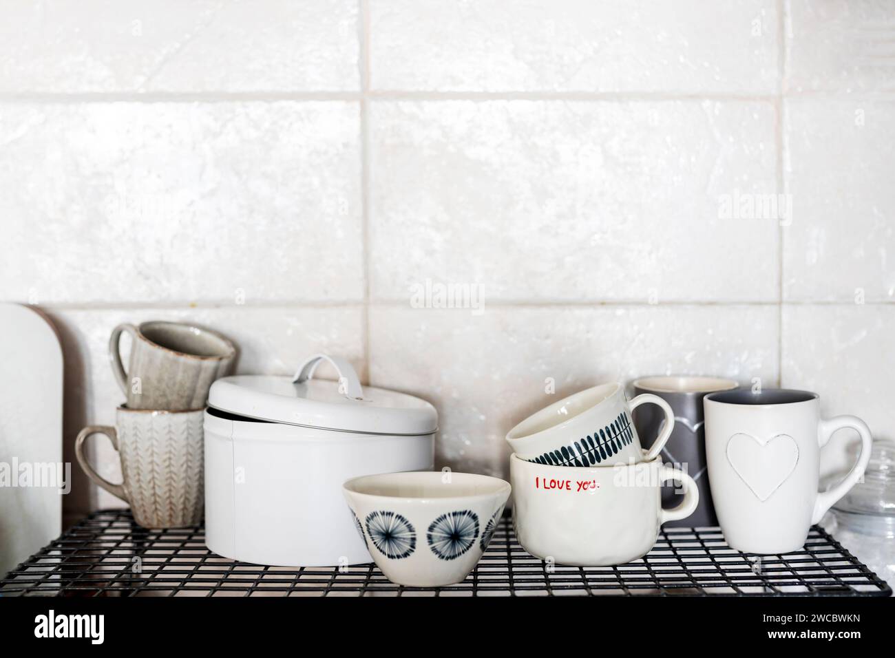 Grau-weiße Tassen mit Herzen und der Inschrift - I love you auf einem Regal in der Küche vor dem Hintergrund einer grau gekachelten Wand. Stockfoto