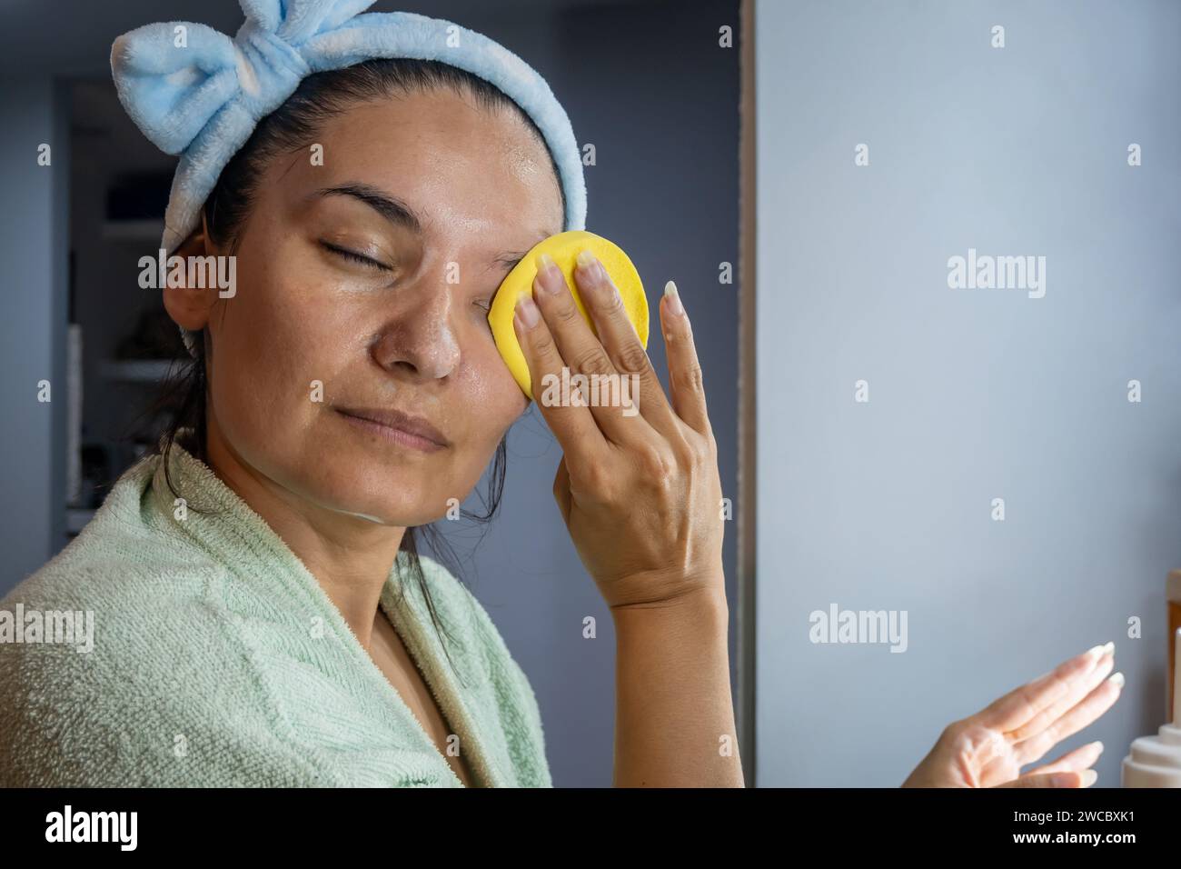 Frau, die ihr Gesicht vor dem Frisiertisch mit einem Schwamm putzt, bevor sie schlafen geht. Stockfoto